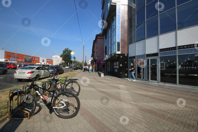 Скачать Беларусь, Минск - 22.09.2024: Оживленный городской тротуар, освещенный теплым послеполуденным солнцем, с припаркованными велосипедами и оживленными пешеходами фотосток Ozero