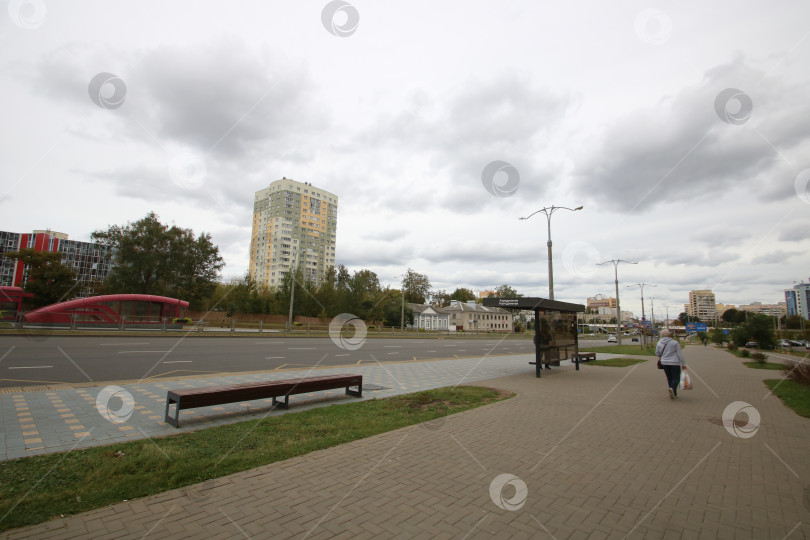 Скачать Беларусь, Минск - 22.09.2024: Обычная городская жизнь пешеходов. Одинокий человек проходит мимо автобусной остановки к многоквартирному дому фотосток Ozero