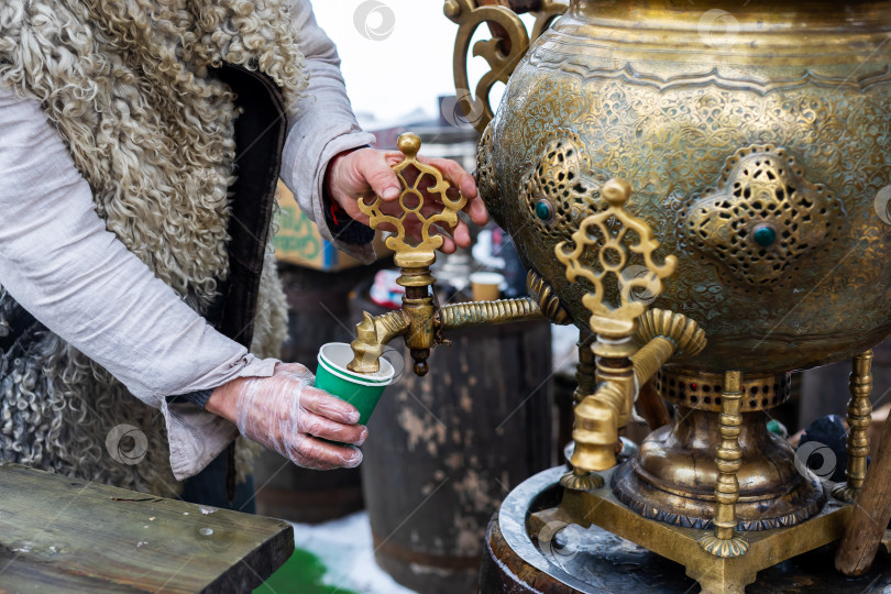 Скачать Старинное мастерство демонстрируется, когда теплый чай льется из богато украшенного самовара на зимнем рынке фотосток Ozero