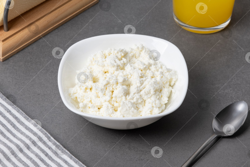 Скачать Сливочный творожный сыр подается в белой миске на сером столе, рядом со стаканом сока и ложкой фотосток Ozero