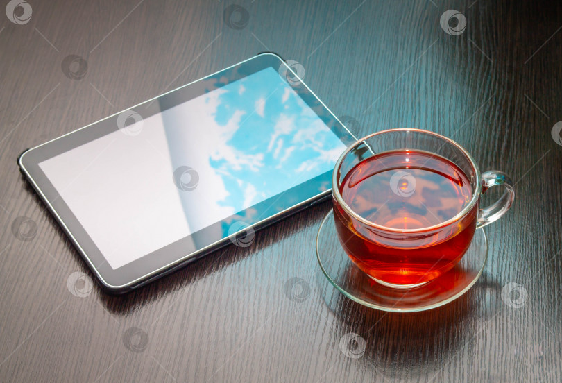 Скачать пейте черный чай в кружке из прозрачного стекла на блюдце рядом с планшетом на деревянном столе фотосток Ozero