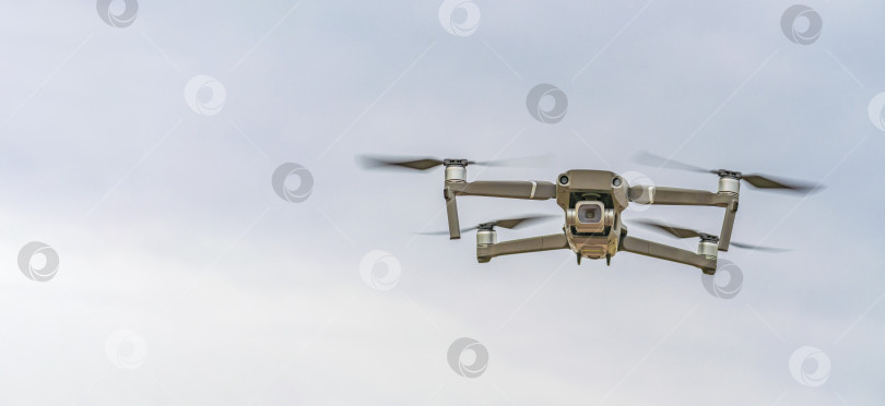 Скачать Маленький квадрокоптер (беспилотник) летит на высоте на фоне серого неба, а камера направлена на фотографа. фотосток Ozero
