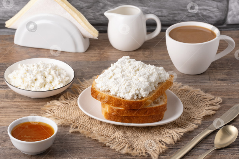 Скачать Сервировка завтрака с хлебом, творогом, кофе и джемом на деревянном столе в уютной кухонной обстановке фотосток Ozero