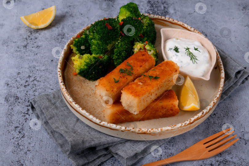 Скачать Хрустящие рыбные палочки в панировке подаются с брокколи, приготовленной на пару, йогуртовым соусом и долькой лимона фотосток Ozero