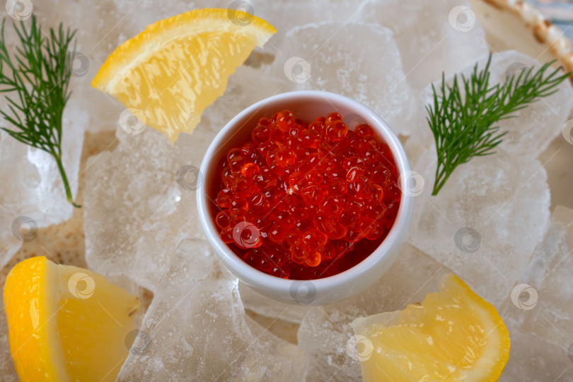 Скачать Красная икра в белой миске, дольки лимона и веточка укропа на подносе со льдом крупным планом фотосток Ozero