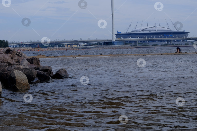 Скачать Газпром Арена - стадион в городе, Финский залив с легким волнением на поверхности и береговые валуны фотосток Ozero
