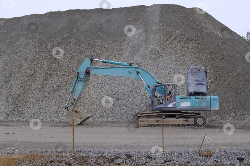 Скачать Поврежденный экскаватор на фоне кучи гравия. Строительные машины и механизмы. фотосток Ozero