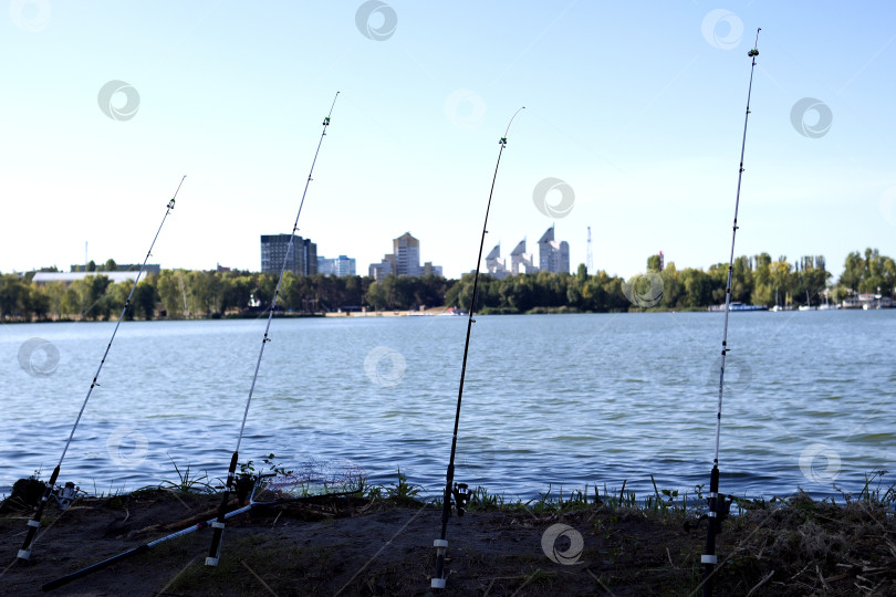 Скачать Рыболовные удочки на фоне водоема и города в лучах утреннего солнца. фотосток Ozero