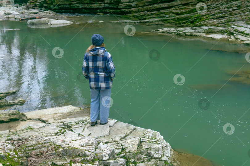 Скачать молодая женщина в клетчатом жакете стоит на камне у реки. фотосток Ozero