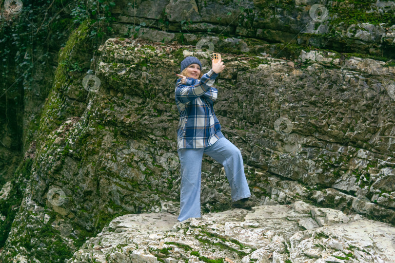 Скачать молодая женщина в клетчатой куртке и джинсах делает селфи на берегу горного озера фотосток Ozero