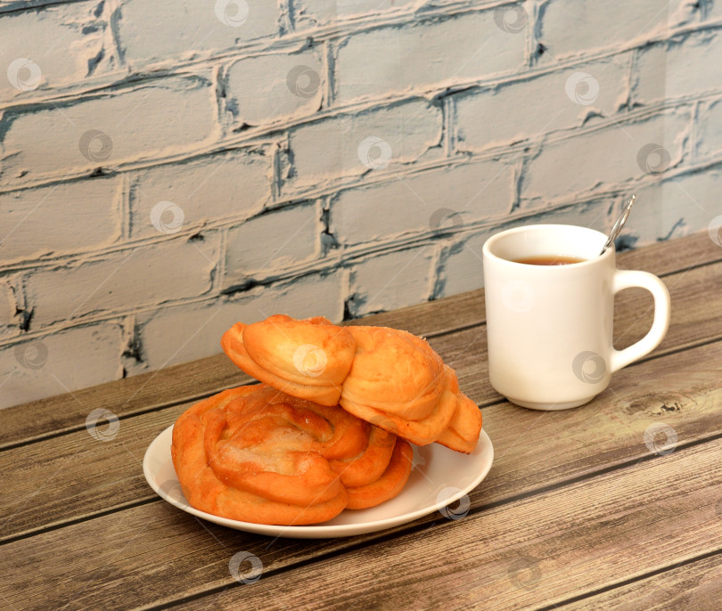 Скачать Два сахарных кренделька на тарелке и чашка горячего черного чая на деревянном столе. фотосток Ozero