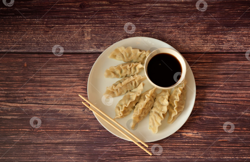 Скачать Вонтоны, китайские пельмени на пару, чашка соевого соуса и палочки для еды на деревянном столе. фотосток Ozero