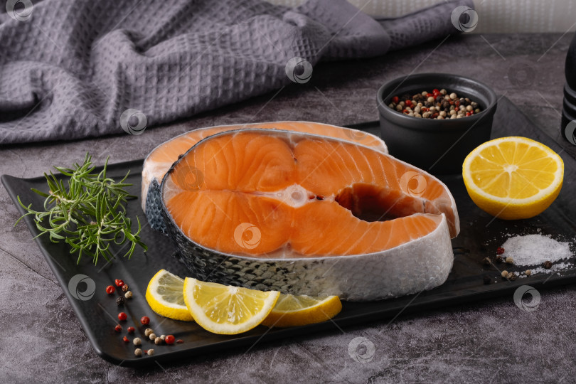 Скачать Филе свежего лосося с ломтиками лимона и перцем, готовое к приготовлению на черном блюде в кухонных условиях фотосток Ozero