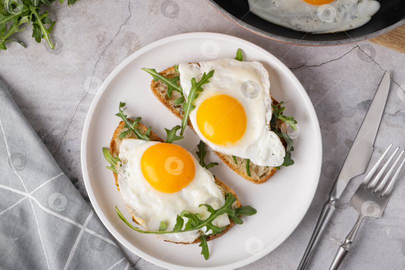Скачать Завтрак с яйцами на тостах и свежей рукколой подается на белой тарелке на кухне фотосток Ozero