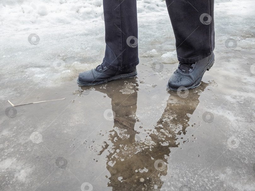 Скачать Темные ботинки осторожно ступают по слякотной луже. фотосток Ozero