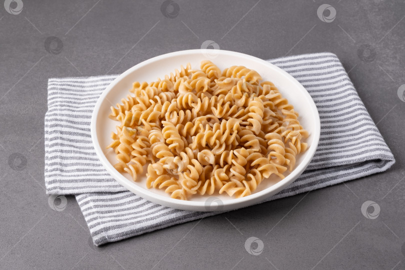 Скачать Паста подается на белой тарелке, накрытой полосатым кухонным полотенцем, к обеденному столу в дневное время фотосток Ozero