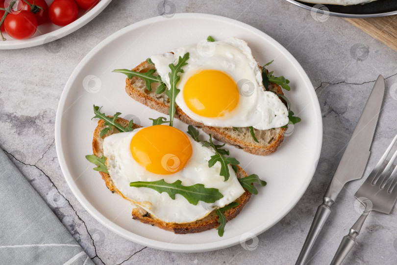 Скачать Завтрак с яйцами на тостах и свежей рукколой подается на белой тарелке на кухне фотосток Ozero