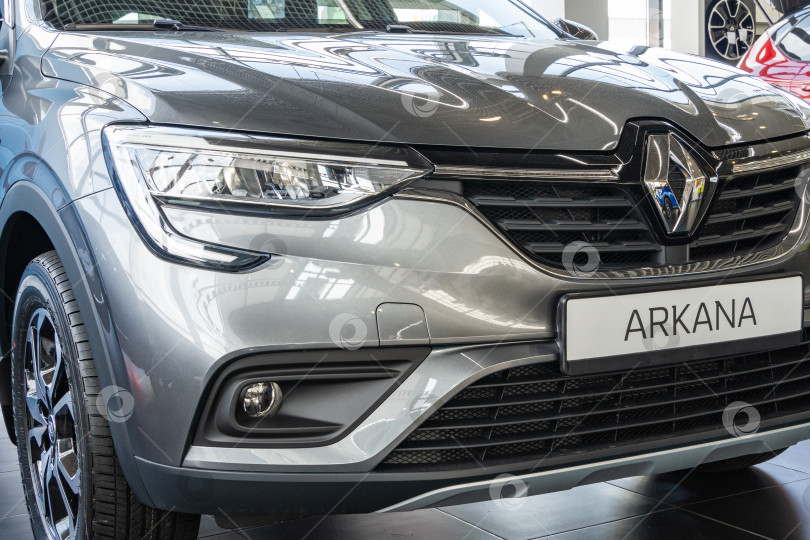 Скачать Серый внедорожник Renault Arkana в автосалоне Renault. Крупный план правой фары, фонаря, черного колеса и решетки радиатора с эмблемой. Автосалон Renault в Мега Адыгея фотосток Ozero