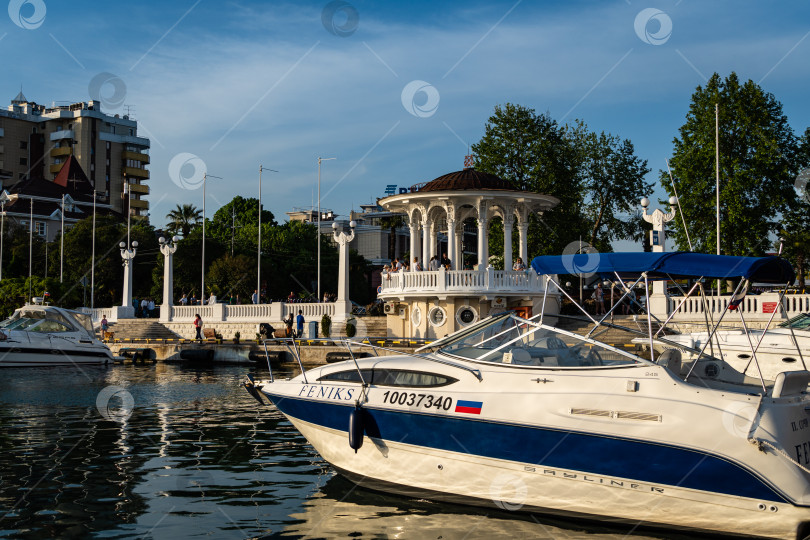 Скачать Сочинский морской торговый порт на закате. Теплоходы и яхты у причала перед главным зданием Морского вокзала. Крупный план. Спокойное Черное море. Отражение яхт в воде. фотосток Ozero