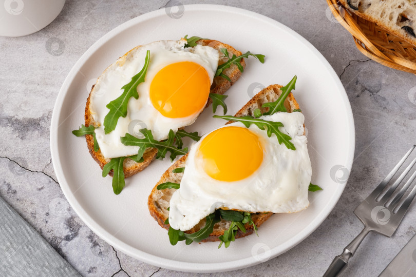 Скачать Завтрак с яйцами на тостах и свежей рукколой подается на белой тарелке на кухне фотосток Ozero
