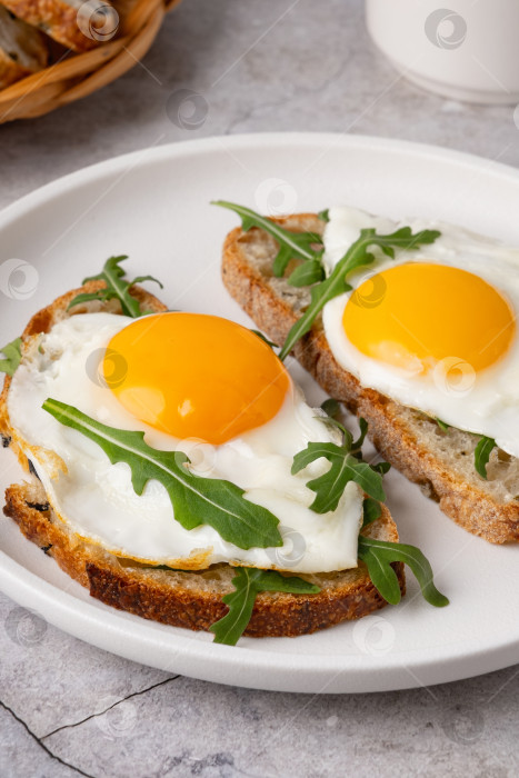 Скачать Завтрак с яйцами на тостах и свежей рукколой подается на белой тарелке на кухне фотосток Ozero