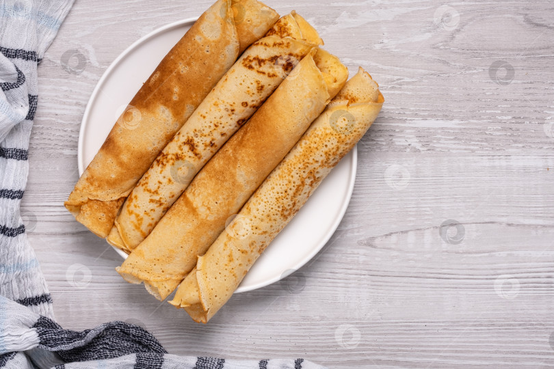 Скачать Стопка тонких блинчиков на белой тарелке, поставленная на деревянный стол у каменной стены на кухне в светлое время суток фотосток Ozero