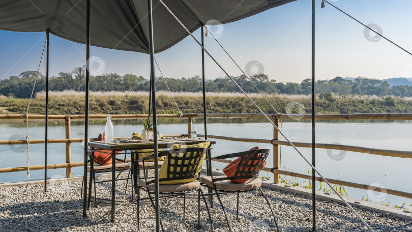 Скачать На посыпанной гравием террасе есть накрытый стол и стулья с подушками. фотосток Ozero