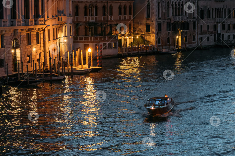 Скачать Одинокая моторная лодка плывет по Большому каналу в Венеции в сиянии огней на фоне голубой воды летним вечером. Концепция романтических туристических поездок по древнему городу Италии. Копировальное пространство фотосток Ozero