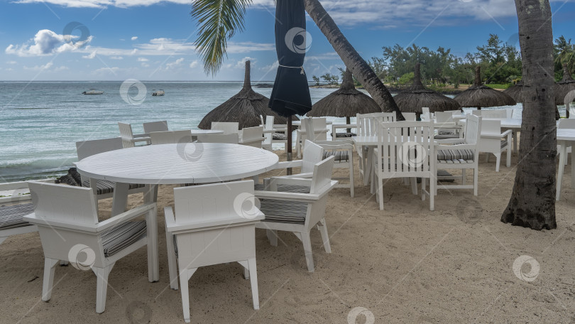 Скачать Кафе на открытом воздухе у моря. Белые пластиковые столы и стулья на песчаном пляже. фотосток Ozero