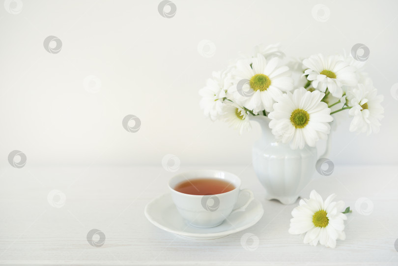 Скачать Букет белых цветов и чашка с чаем на белом деревянном столе, копировальное пространство. Травяной чай и букет из цветов маргаритки или ромашки на белом фоне фотосток Ozero