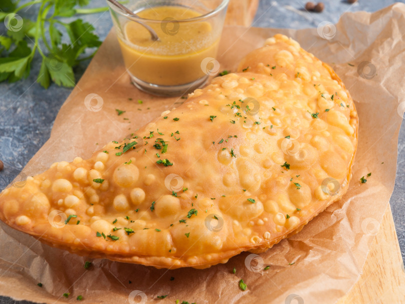 Скачать чебурек с мясом и горчичной заправкой, украшенный зеленью, на пергаменте фотосток Ozero