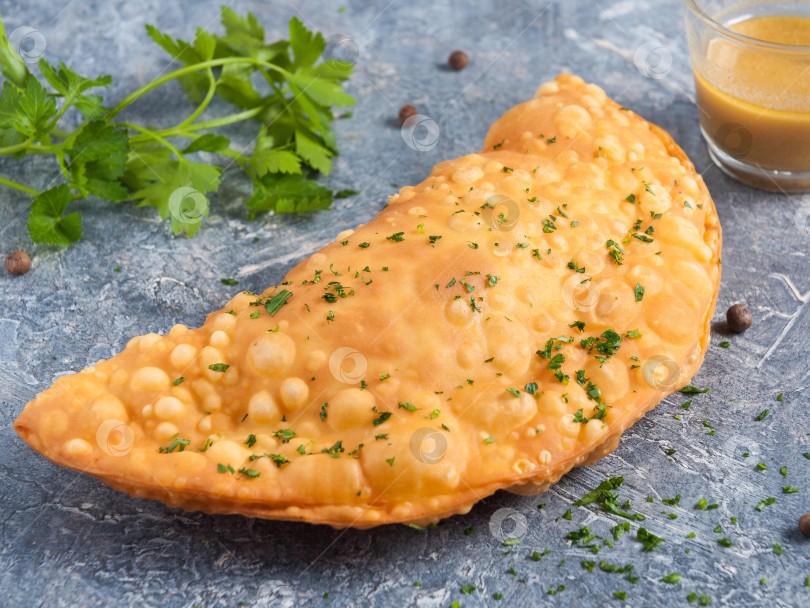 Скачать чебурек с мясом и горчичной заправкой, украшенный зеленью на сером фоне фотосток Ozero