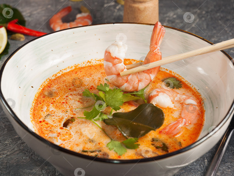 Скачать вкусный азиатский суп Том Ям. Мужчина держит креветку палочками для еды фотосток Ozero