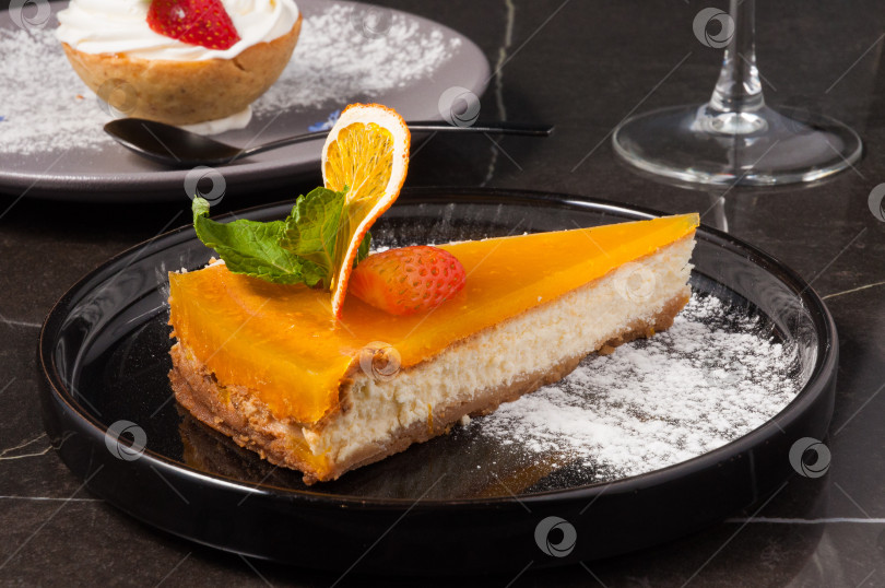 Скачать вкусный десерт -апельсиновый чизкейк на черной тарелке фотосток Ozero