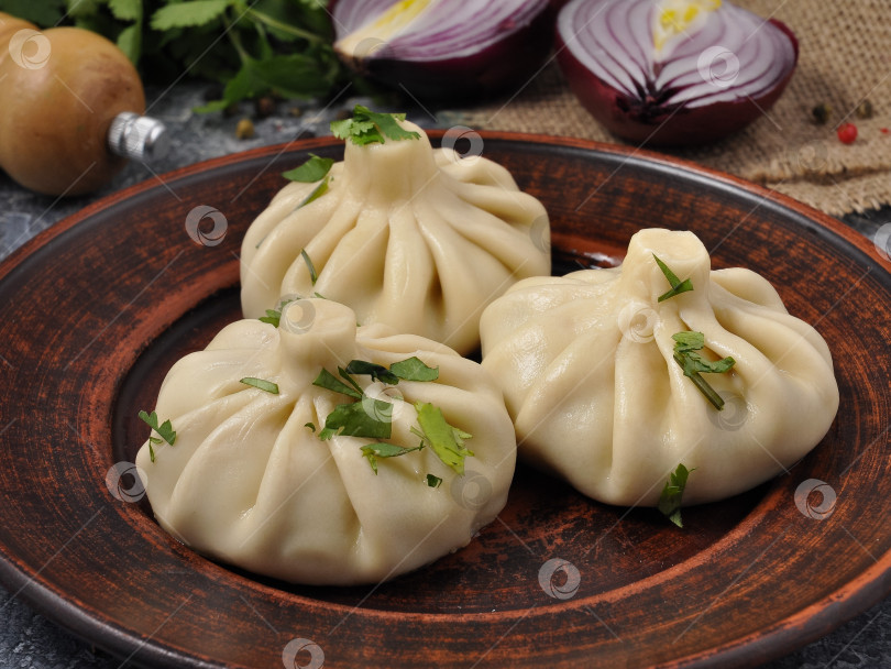 Скачать хинкали с мясом на глиняной тарелке, украшенные зеленью фотосток Ozero
