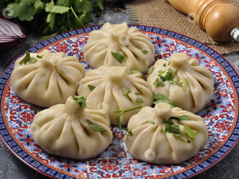 Скачать хинкали с мясом на глиняной тарелке, украшенные зеленью фотосток Ozero