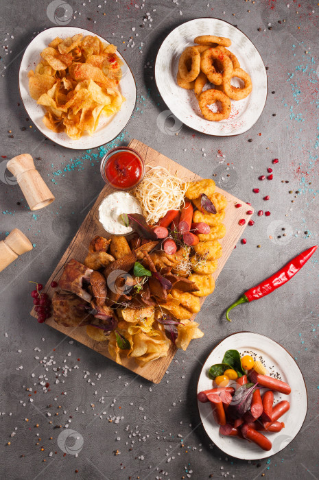 Скачать ассорти закусок к пиву: чипсы, сосиски, луковые кольца, куриные наггетсы, гренки, копченые ребрышки, куриные крылышки, томатно-чесночный соус фотосток Ozero