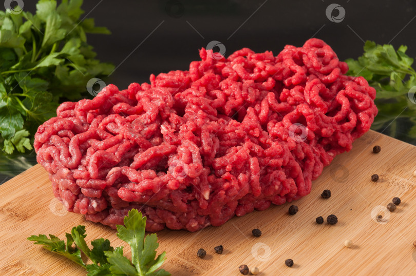 Скачать сырой мясной фарш, украшенный зеленью, на деревянной доске фотосток Ozero