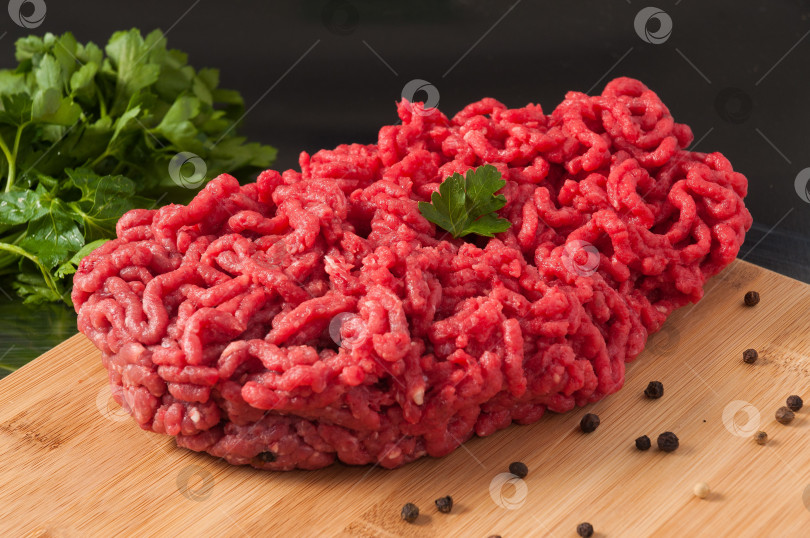 Скачать сырой мясной фарш, украшенный зеленью, на деревянной доске фотосток Ozero