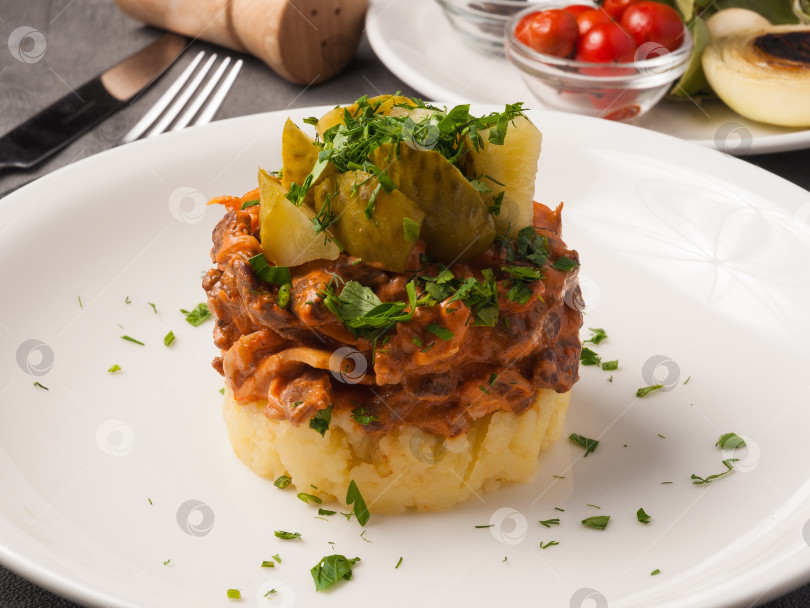 Скачать бефстроганов с картофельным пюре и солеными огурцами на белой тарелке фотосток Ozero