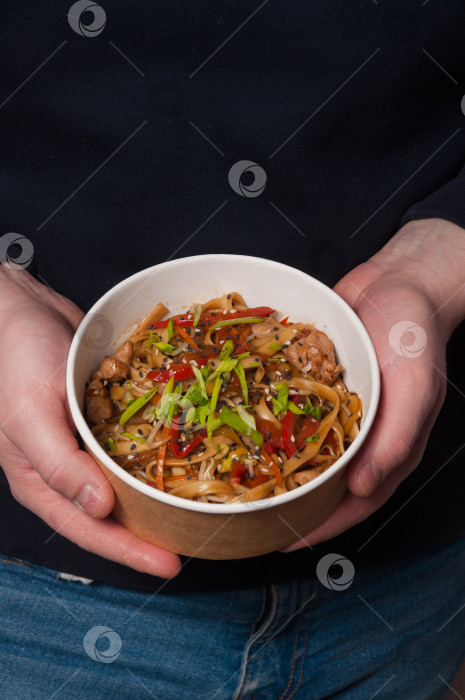 Скачать мужчина держит в руках миску с лапшой удон с курицей и овощами фотосток Ozero