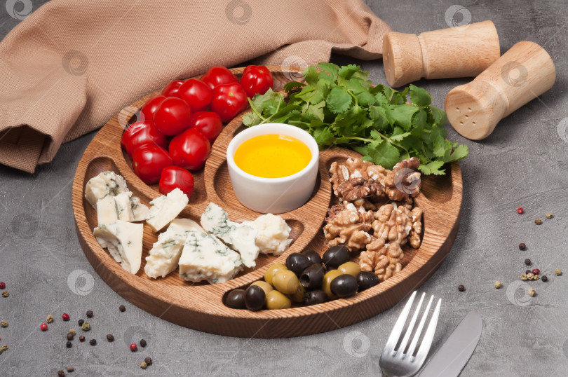 Скачать деревянная тарелка с сыром, орехами, помидорами и оливками фотосток Ozero