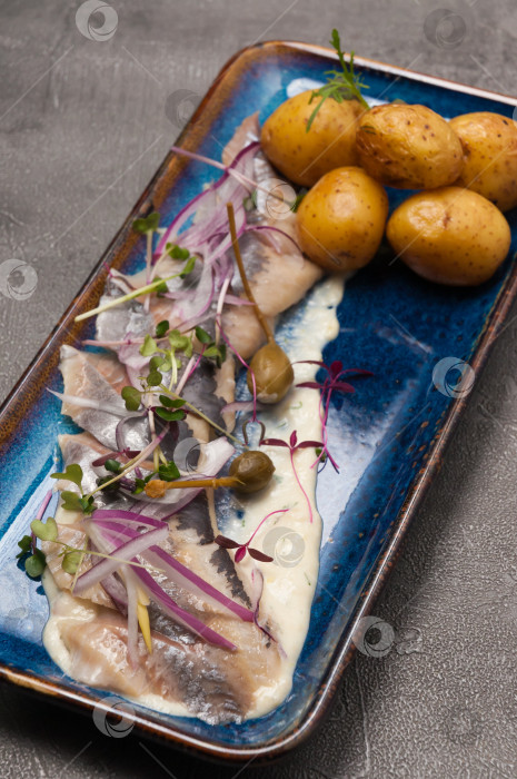 Скачать соленая сельдь с картофелем в кожуре, украшенная каперсами и красным луком. крупный план фотосток Ozero