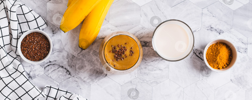 Скачать Смесь банана, куркумы и растительного молока в стакане на столешнице посмотреть веб-баннер фотосток Ozero