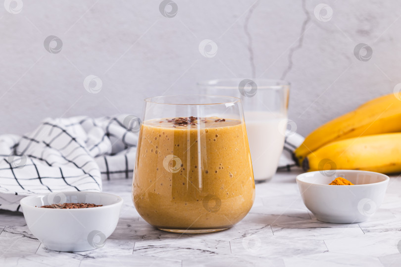 Скачать Смузи из кокосового молока, банана, куркумы и семян льна в стакане на столе фотосток Ozero