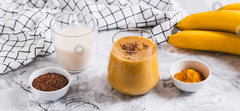 Скачать Смузи из кокосового молока, банана, куркумы и семян льна в стеклянной сетчатой упаковке фотосток Ozero
