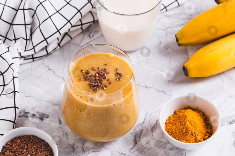 Скачать Смешайте банан, куркуму и растительное молоко в стакане на столе фотосток Ozero