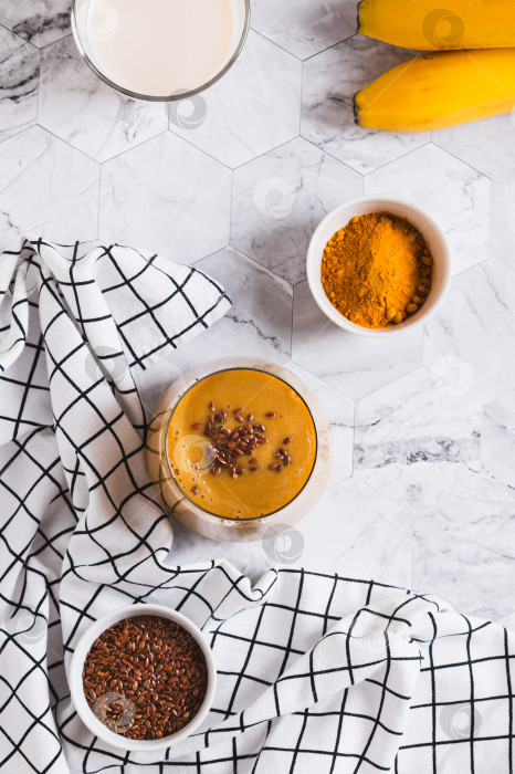 Скачать Смешайте банан, куркуму и растительное молоко в стакане, поставьте его вертикально на стол фотосток Ozero