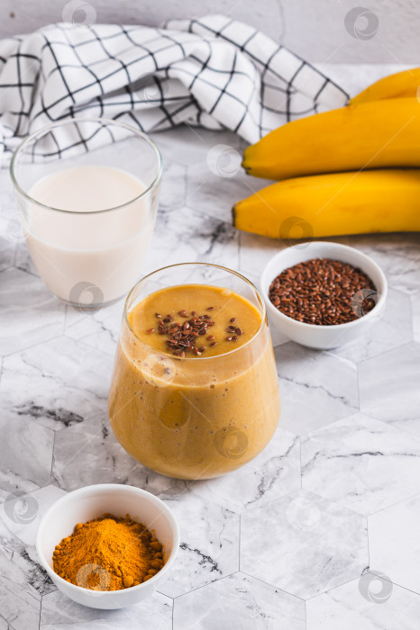Скачать Смешайте банан, куркуму и растительное молоко в стакане и поставьте на стол вертикально фотосток Ozero