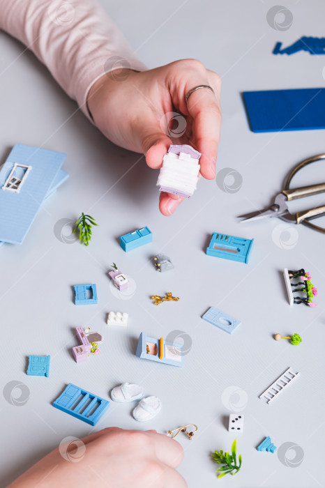 Скачать Миниатюрные детали и мебель для игрушечного домика в руках детей на синем фоне по вертикали фотосток Ozero
